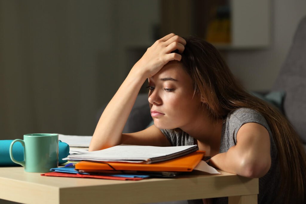 Exhausted young woman resting head on hand while struggling to focus on notes late at night, a sign of ADHD in women