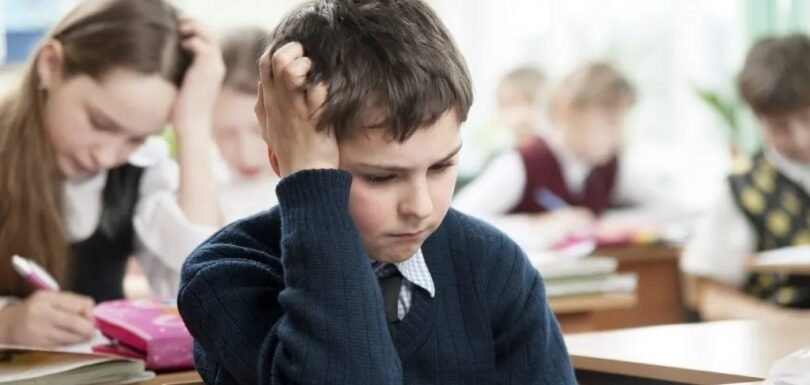 School boy resting head on hand, struggling to concentrate on classwork — a sign of ADHD in children