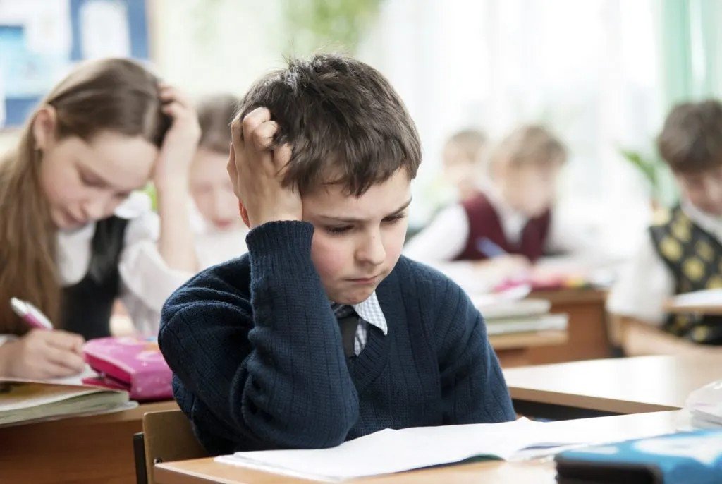 School boy resting head on hand, struggling to concentrate on classwork — a sign of ADHD in children